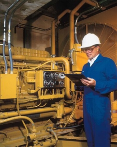 A technician in a white hard hat inspects a large, yellow generator.