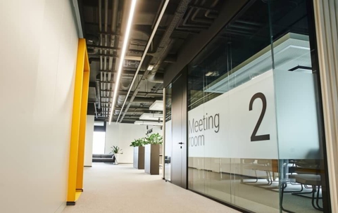 Hallway view of a bright, modern office space with glass-enclosed meeting room.